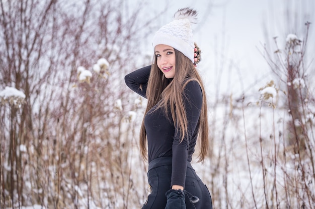 Uma linda garota sorridente com roupas pretas e um chapéu branco de malha no inverno