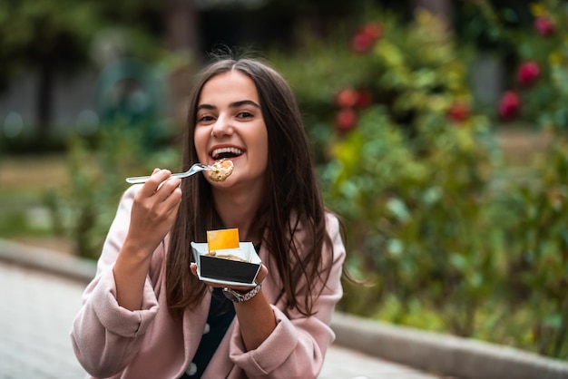 Uma linda garota sorridente come poffertjes frescos enquanto passeia pela cidade Foco seletivo