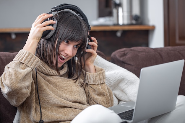 Uma linda garota sorridente em fones de ouvido ouve música e olha para a tela do laptop.