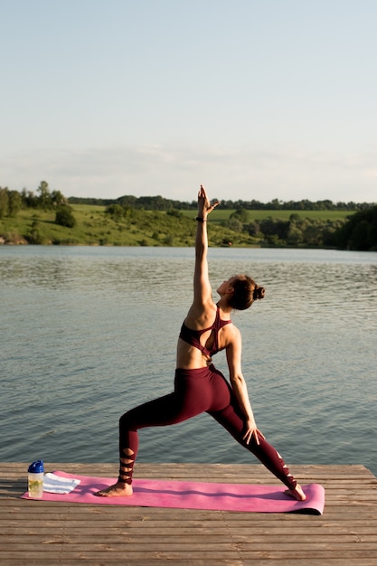 Uma linda garota treina na margem do rio. Ela faz exercícios de ioga, faz asanas.