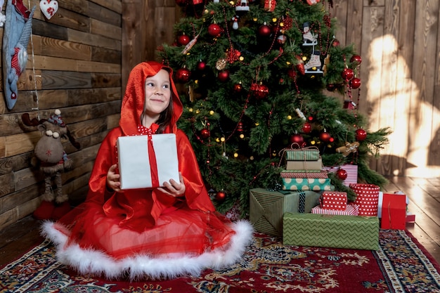 Uma linda garotinha ao lado da árvore de Natal fica feliz com um presente