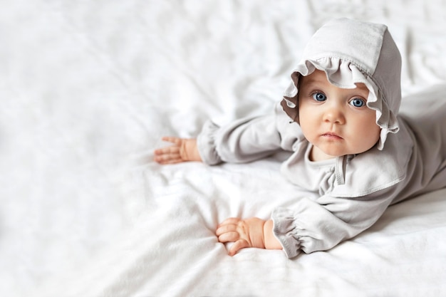 Uma linda garotinha com grandes olhos azuis deitada em um lençol branco em casa na cama