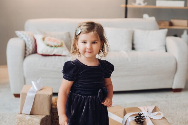 Uma linda garotinha com um vestido sentada cercada por muitas caixas de presentes de natal e quer abri-los