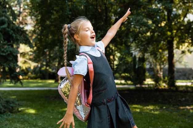 Uma linda garotinha com uma mochila rosa está andando no parque e se divertindo. uniforme escolar.