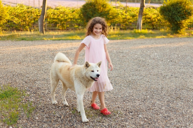 Uma linda garotinha de vestido rosa abraça seu cachorro favorito durante uma caminhada de verão Vista horizontal