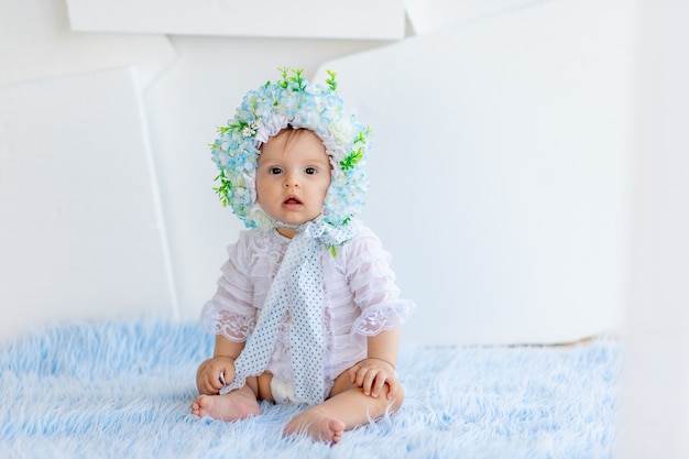 Uma linda garotinha deitada em um tapete azul fofo com um chapéu feito de flores e olhando para a câmera