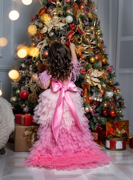 Uma linda garotinha em um vestido elegante decorando a árvore de Natal