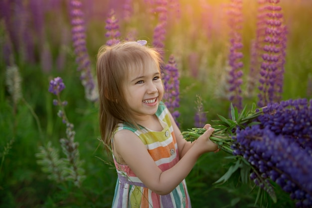 Uma linda garotinha está rindo e acenando com um monte de tremoços em um campo de flores ao pôr do sol