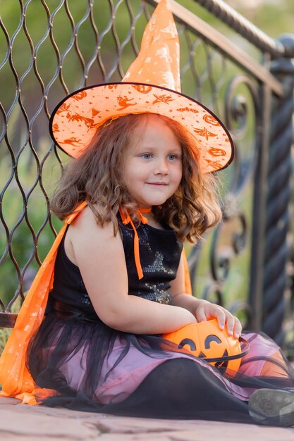 Uma linda garotinha fantasiada de bruxa para o Halloween caminha no parque em uma cesta de doces no