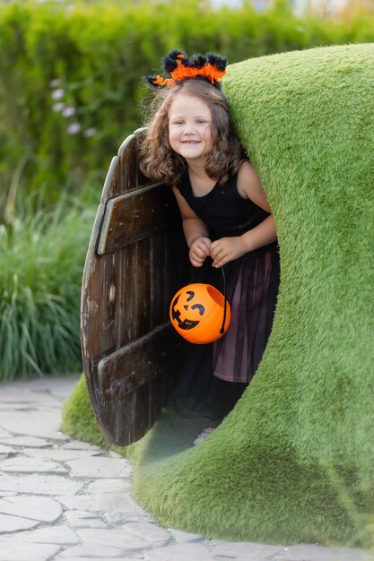 Foto uma linda garotinha fantasiada de bruxa para o halloween caminha no parque em uma cesta de doces no