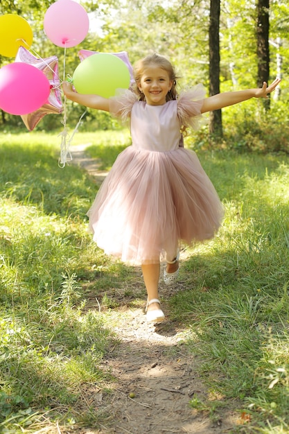 uma linda garotinha loira com um vestido rosa e balões caminhando no parque