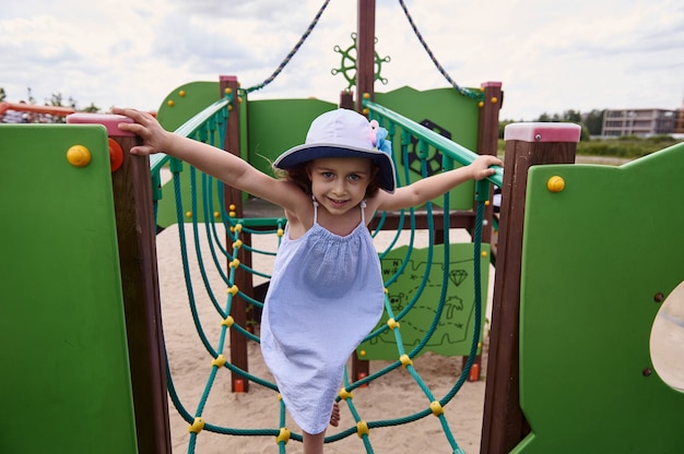 Uma linda garotinha sobe nas cordas do parquinho do acampamento infantil de verão. Ativo durante as férias escolares de verão