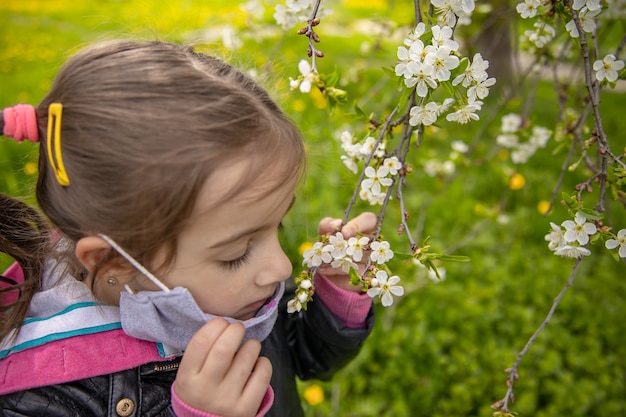 Uma linda garotinha tirou a máscara para sentir o cheiro das flores da primavera na árvore.