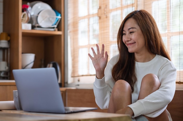 Uma linda jovem asiática freelancer usando laptop para videochamada e trabalhando online em casa