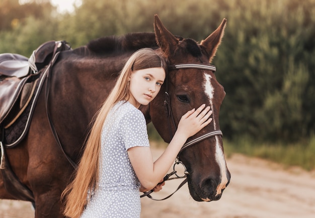 Uma linda jovem com cabelo comprido fica ao lado de um cavalo na natureza no verão