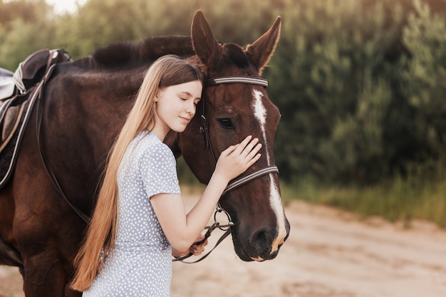 Uma linda jovem com cabelo comprido fica ao lado de um cavalo na natureza no verão