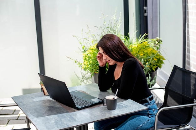 Uma linda jovem com um laptop se senta em uma mesa e olha para o manitor