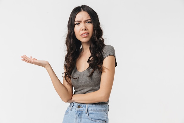 Uma linda jovem confusa descontente posando isolado sobre uma parede branca.