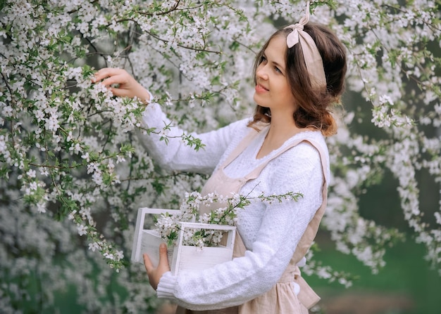 Uma linda jovem de avental aproveita a vida em um jardim florescente de primavera com árvores floridas