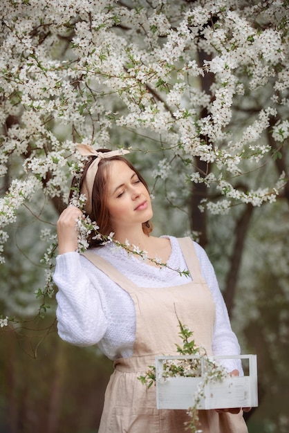 Uma linda jovem de avental aproveita a vida em um jardim florescente de primavera com árvores floridas