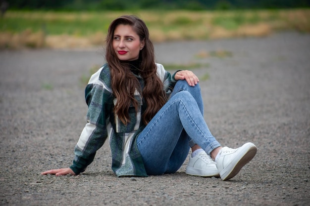 Uma linda jovem de jeans senta-se na estrada