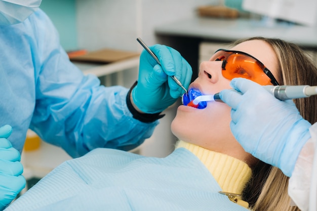 Uma linda jovem de óculos odontológicos trata os dentes no dentista com luz ultravioleta. obturação de dentes.