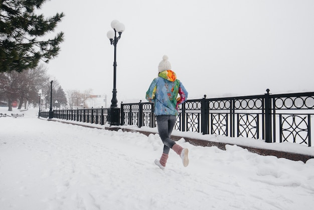 Uma linda jovem está correndo em um dia gelado e com neve. Esportes, estilo de vida saudável