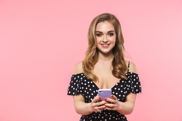 uma linda jovem feliz posando isolada sobre uma parede rosa usando um telefone celular