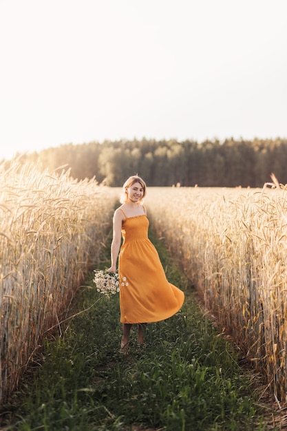 Uma linda jovem fica em um campo de trigo e tem um buquê de margaridas nas mãos.