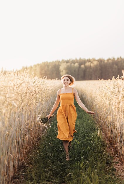 Uma linda jovem fica em um campo de trigo e tem um buquê de margaridas nas mãos.