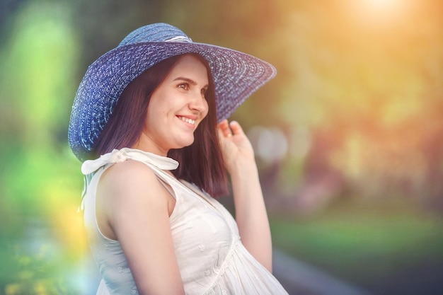 Uma linda jovem grávida de chapéu azul sorri e desvia o olhar