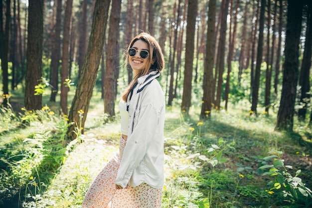 Uma linda jovem hippie caminha na floresta de verão, ri, dança e aproveita a vida e a natureza