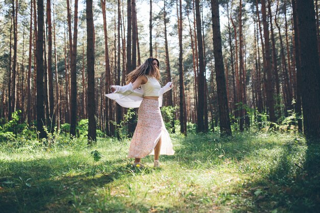 Uma linda jovem hippie caminha na floresta de verão, ri, dança e aproveita a vida e a natureza