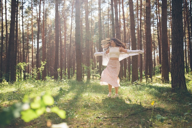 Uma linda jovem hippie caminha na floresta de verão, ri, dança e aproveita a vida e a natureza