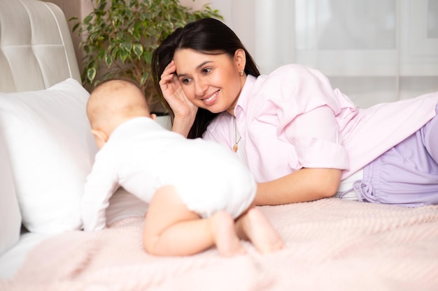 Uma linda jovem mãe brinca e abraça seu bebê na cama Amo a maternidade Estilo de vida