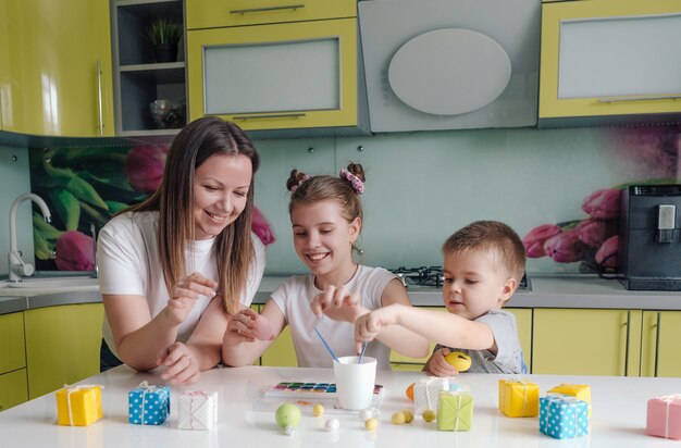 Uma linda jovem mãe com dois filhos decorou ovos de páscoa tradicionais com tinta brilhante, o conceito de uma família feliz se preparando para o feriado de páscoa