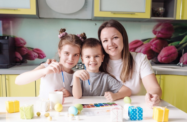 Uma linda jovem mãe com dois filhos decorou ovos de páscoa tradicionais com tinta brilhante, o conceito de uma família feliz se preparando para o feriado de páscoa