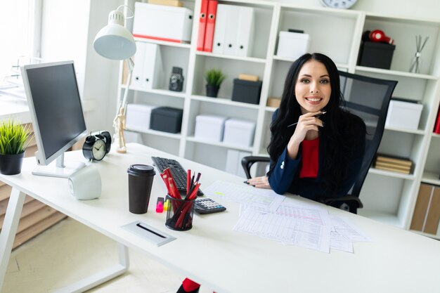 Uma linda jovem senta-se no escritório à mesa e tem um lápis na mão.