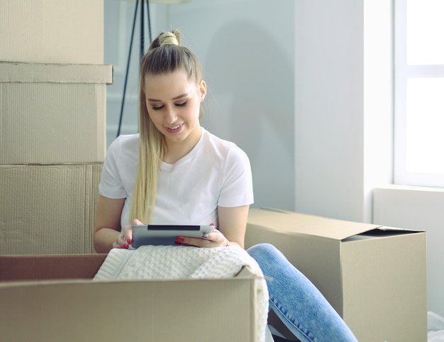 Uma linda jovem solteira desembalando caixas e se mudando para uma nova casa Uma mulher olha para aqui tablet