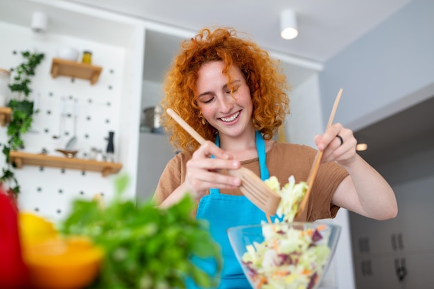 Uma linda jovem sorridente na cozinha está preparando uma salada vegana em roupas casuais