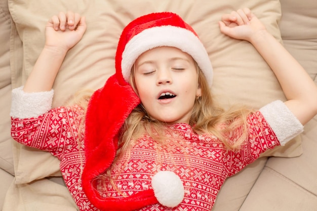 uma linda loira com um chapéu de Papai Noel e pijama de ano novo está dormindo na cama