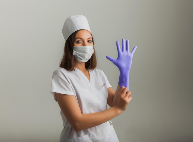 Uma linda médica ou enfermeira em uma máscara protetora e luvas de borracha sobre um fundo claro com copyspace. Conceito de saúde