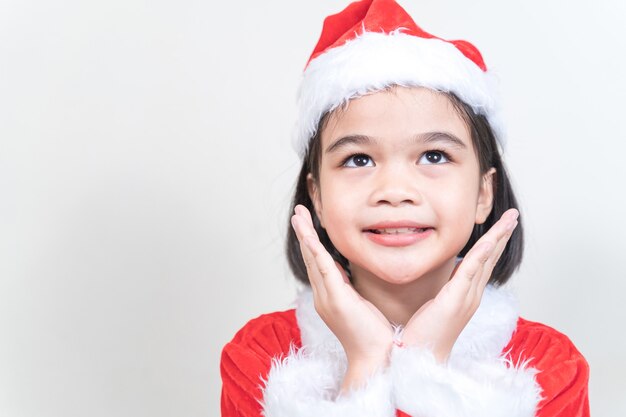 Uma linda menina asiática com um vestido vermelho de Papai Noel, decorando a árvore de Natal na véspera de Natal