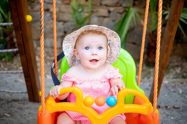 Uma linda menina balançando em um balanço e rindo no verão com um chapéu-panamá