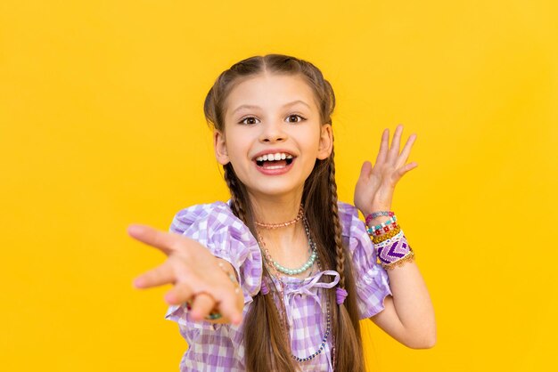 Foto uma linda menina colocou muitas pulseiras de contas coloridas e estende a mão com as palmas das mãos perlas para crianças e adolescentes fundo isolado amarelo