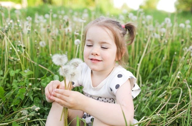 Uma linda menina está sentada na grama em um campo de primavera, entre flores ao ar livre, curtindo a natureza. o conceito de liberdade