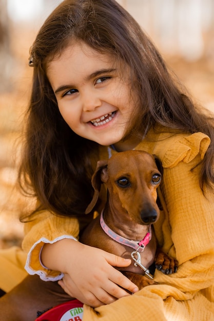 Uma linda menina morena caminha no outono com um cachorro dachshund no parque