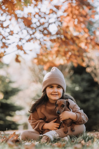 Uma linda menina morena caminha no outono com um cachorro dachshund no parque