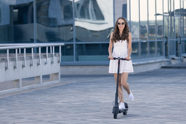 Uma linda morena de vestido leve anda de scooter elétrica pela cidade