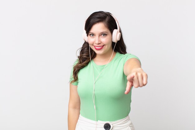 Uma linda mulher apontando para a câmera escolhendo você ouvindo música com fones de ouvido